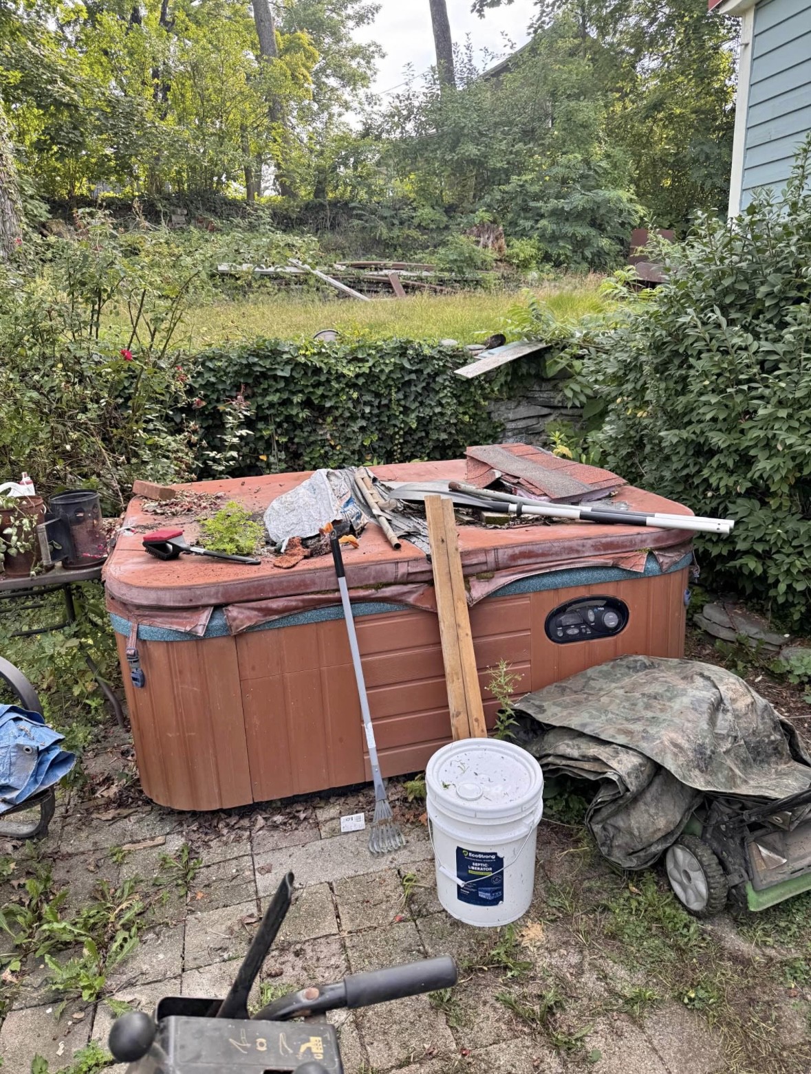 Worn out backyard hot tub surrounded by debris before removal