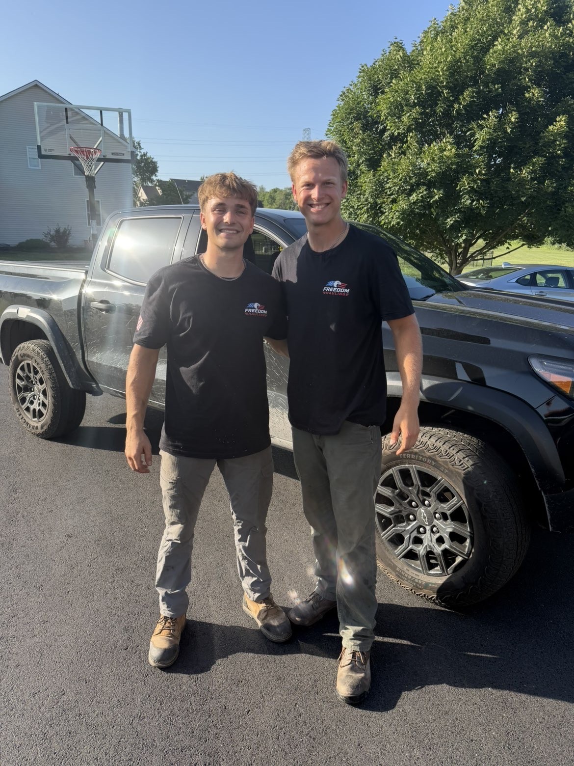 The two owners of Freedom Hauling standing in front of their pickup truck